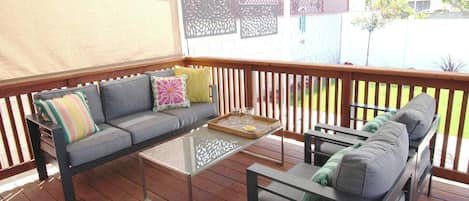 A covered outdoor seating area with a sofa, two side tables, and a small round table.