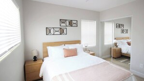 Un dormitorio con cama, mesitas de noche, un espejo y cuadros en la pared.