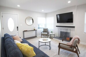 A living room with a sofa, armchair, coffee table, fireplace, TV, and a console table with a mirror. - Greater North Park Home + Fenced Yard (San Diego)