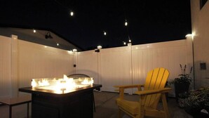 Un patio al aire libre con una parrilla, una silla y luces colgantes.