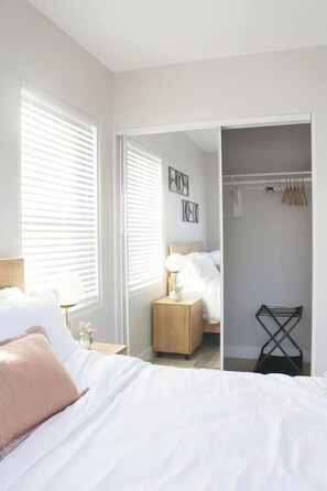 A bedroom with a bed, bedside table, lamp, and a closet with hanging clothes. - Greater North Park Home + Fenced Yard (San Diego)