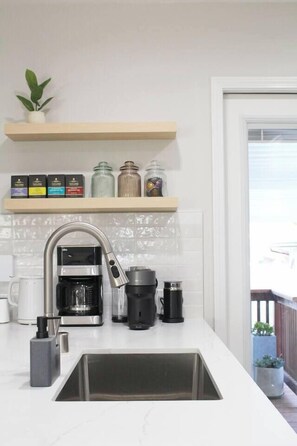 A modern kitchen with a stainless steel sink, a coffee maker, and a range hood. There is a shelf above the sink with jars and a potted plant. - Greater North Park Home + Fenced Yard (San Diego)