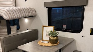 A compact RV interior with a dining area, seating, and a window. - Cozy Family Camper with Bunks (Fayetteville)