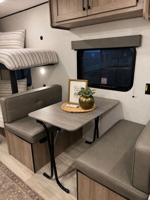 Interior compacto de uma RV com área de refeições, assentos e uma janela.