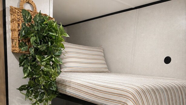 A bunk bed with striped bedding, a hanging plant, and a wall-mounted light fixture. - Cozy Family Camper with Bunks (Fayetteville)
