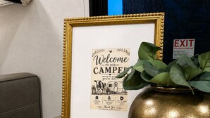 A framed welcome sign, a remote control, and a decorative pot on a woven placemat. - Cozy Family Camper with Bunks (Fayetteville)