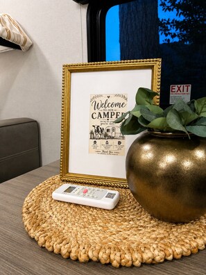 Uma placa de boas-vindas emoldurada, um controle remoto e um vaso decorativo sobre um descanso trançado.