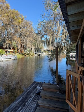 A wooden dock extending into a calm body of water with a view of a cabin and trees with Spanish moss. - Relaxing Getaway at Blue Cypress Lake (Vero Beach)