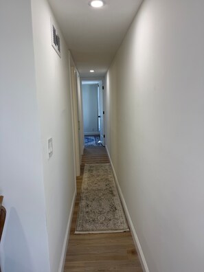 A narrow hallway with wooden flooring and a patterned rug, leading to a room with a door at the end. - Relaxing Getaway at Blue Cypress Lake (Vero Beach)