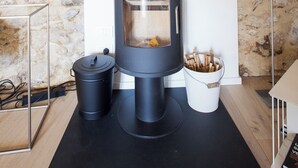 Quarto moderno com parede de pedra, lareira a lenha preta, abajur branco e uma pequena mesa com um livro.