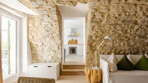 Um interior moderno com paredes de pedra, um sofá branco com almofadas verdes e brancas, uma mesa lateral de madeira redonda e um armário branco.
