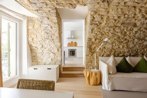 Ein modernes Interieur mit Steinwänden, einem weißen Sofa mit grünen und weißen Kissen, einem runden Holznachttisch und einem weißen Schrank.