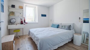 Quarto com cama, escrivaninha, cadeira, janela e espelho.