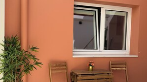 Un área de estar al aire libre con una mesa y dos sillas, una ventana y una planta en maceta.