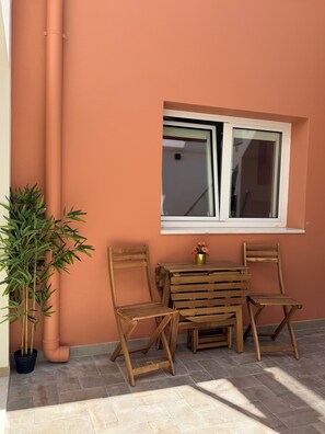 An outdoor seating area with a table and two chairs, a window, and a potted plant. - AL do Barão - Charming House with Private Pool (Vila Real de Santo António)