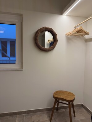 Ein Zimmer mit einem runden Spiegel, einem Holzstuhl und einem Kleiderständer.