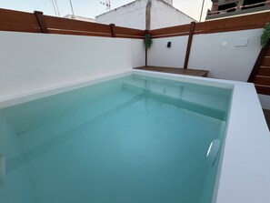 Ein rechteckiger Swimmingpool mit klarem Wasser, umgeben von einem Holenzaun und weißen Wänden.