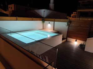 Ein Dachpool mit Glasgeländern, Holzterrasse und einer kleinen Sitzgelegenheit mit Pflanzen.
