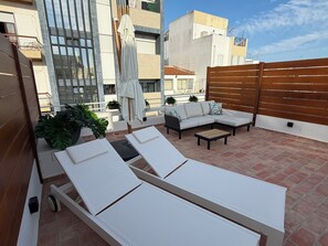 En takterrass med solstolar, en soffa och ett trästaket.