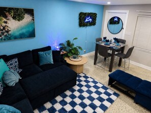 En stue med en sofa, et spisebord med stole, et rundt spejl og en blå væg med et billede.