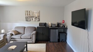 Un espace de vie compact comprenant un canapé, une kitchenette et un téléviseur à écran plat fixé au mur.