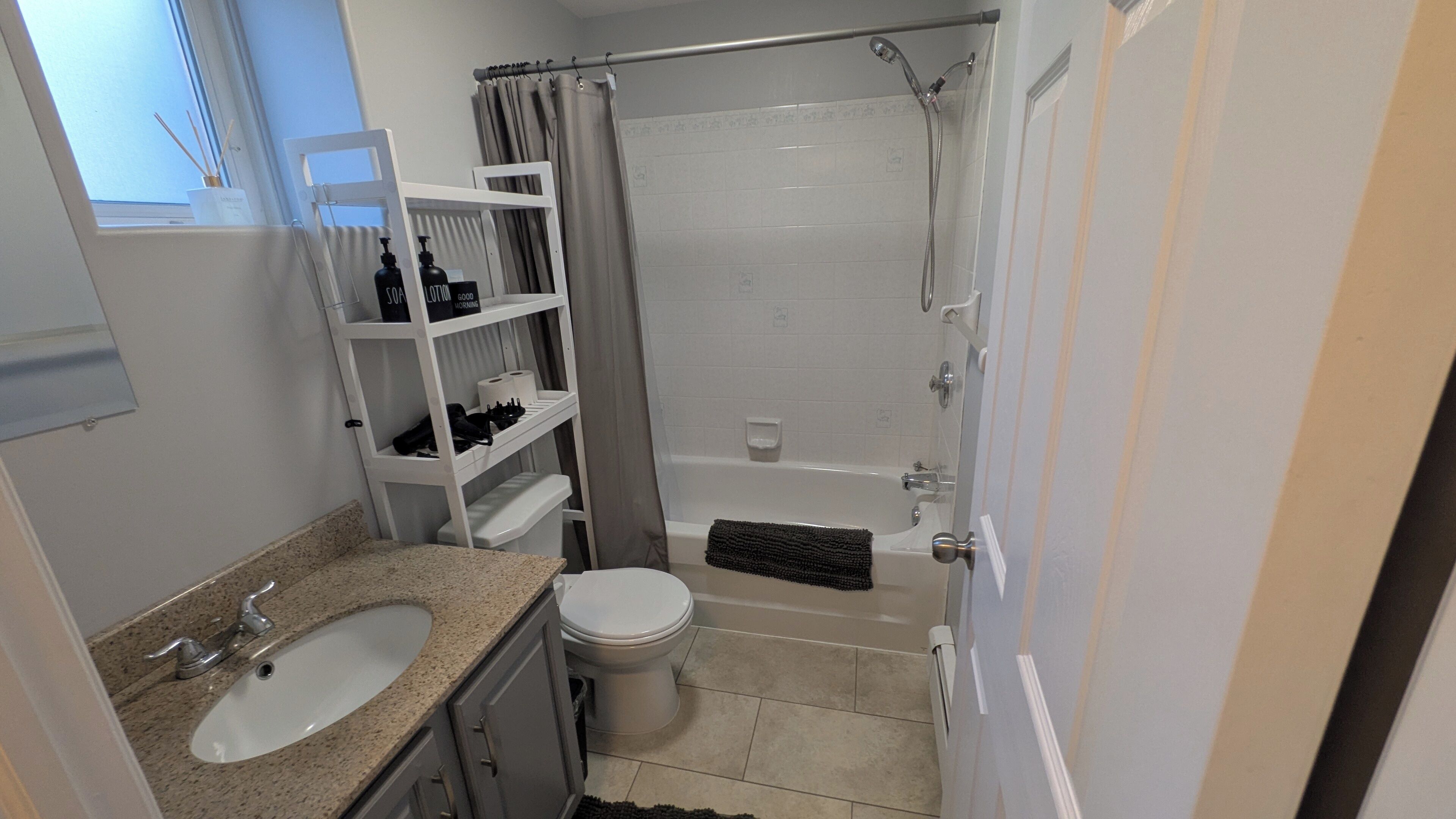 A bathroom with a sink, toilet, shower, and shelves with toiletries.