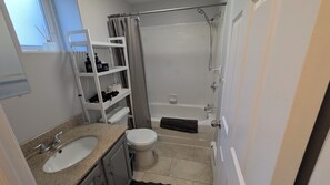 Une salle de bain équipée d’un lavabo, de toilettes, d’une douche et d’étagères où sont rangés les articles de toilette.