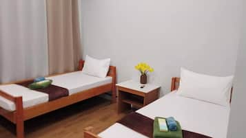 Une chambre d’hôtel avec deux lits simples, des têtes de lit en bois, du linge de lit blanc, une petite table de chevet ornée d’un vase de fleurs et un rideau à la fenêtre.