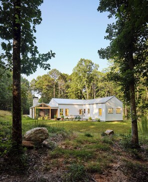 A modern house with a sloped roof, surrounded by a natural landscape with trees and a grassy area. - Architect-Designed Retreat on 5 Acres - Serenbe Trail Access and Detached Studio (Newnan)