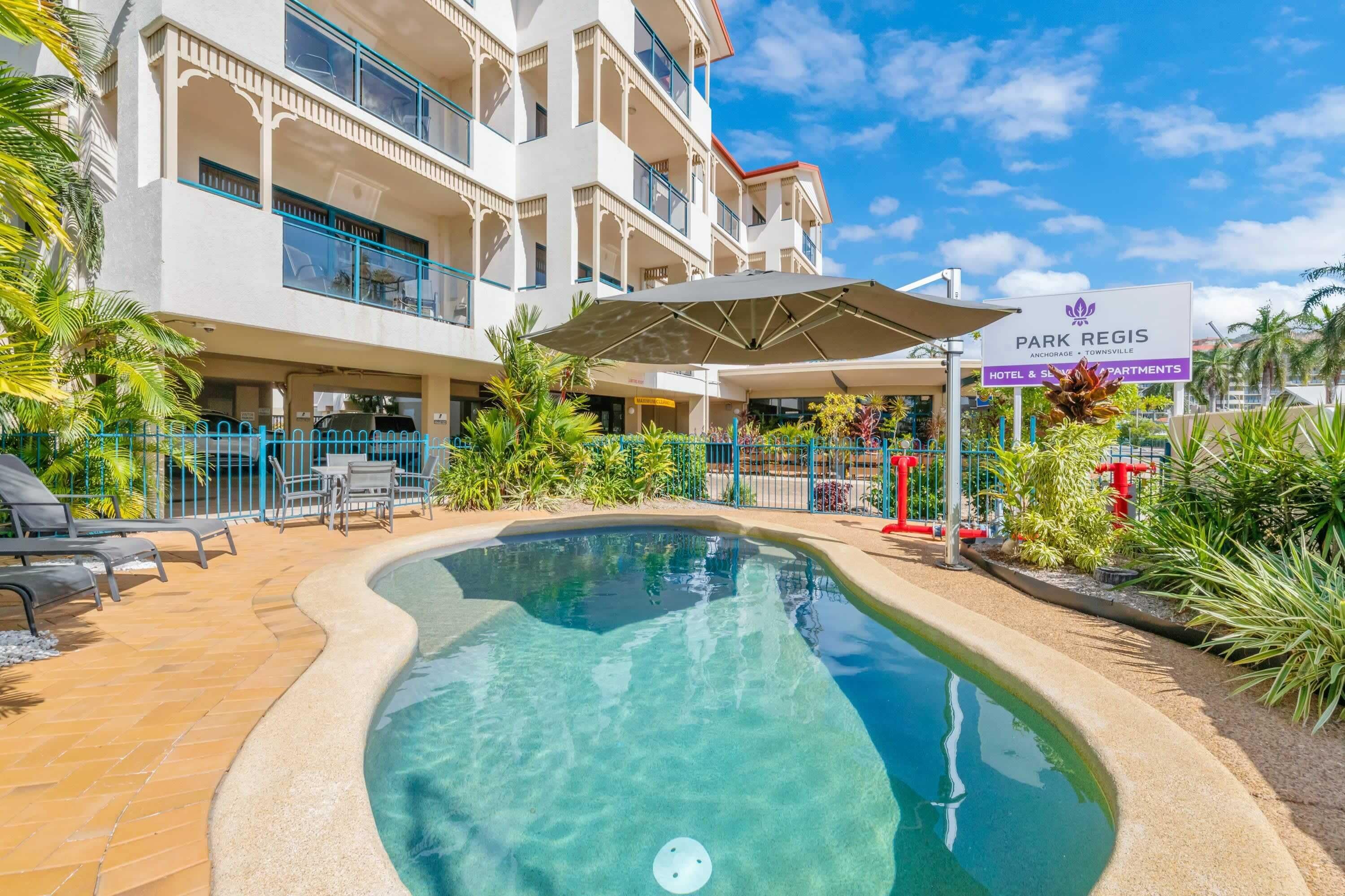 A hotel with a swimming pool, outdoor seating, and a sign indicating it is a Park Regis hotel.