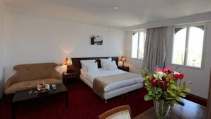 Una habitación de hotel con cama, sofá, una mesita y un jarrón de flores.