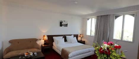 Una habitación de hotel con cama, sofá, una mesita y un jarrón de flores.
