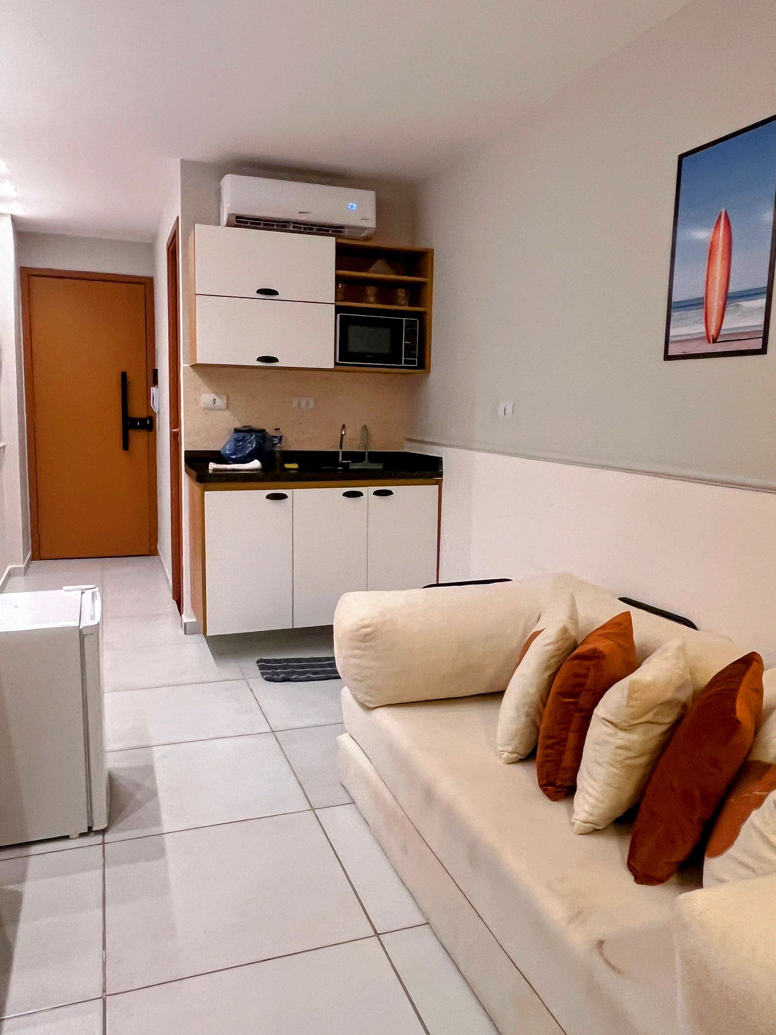 Ett kompakt bostadsutrymme med ett litet kök, en soffa med kuddar och en dörr som leder till ett annat rum.