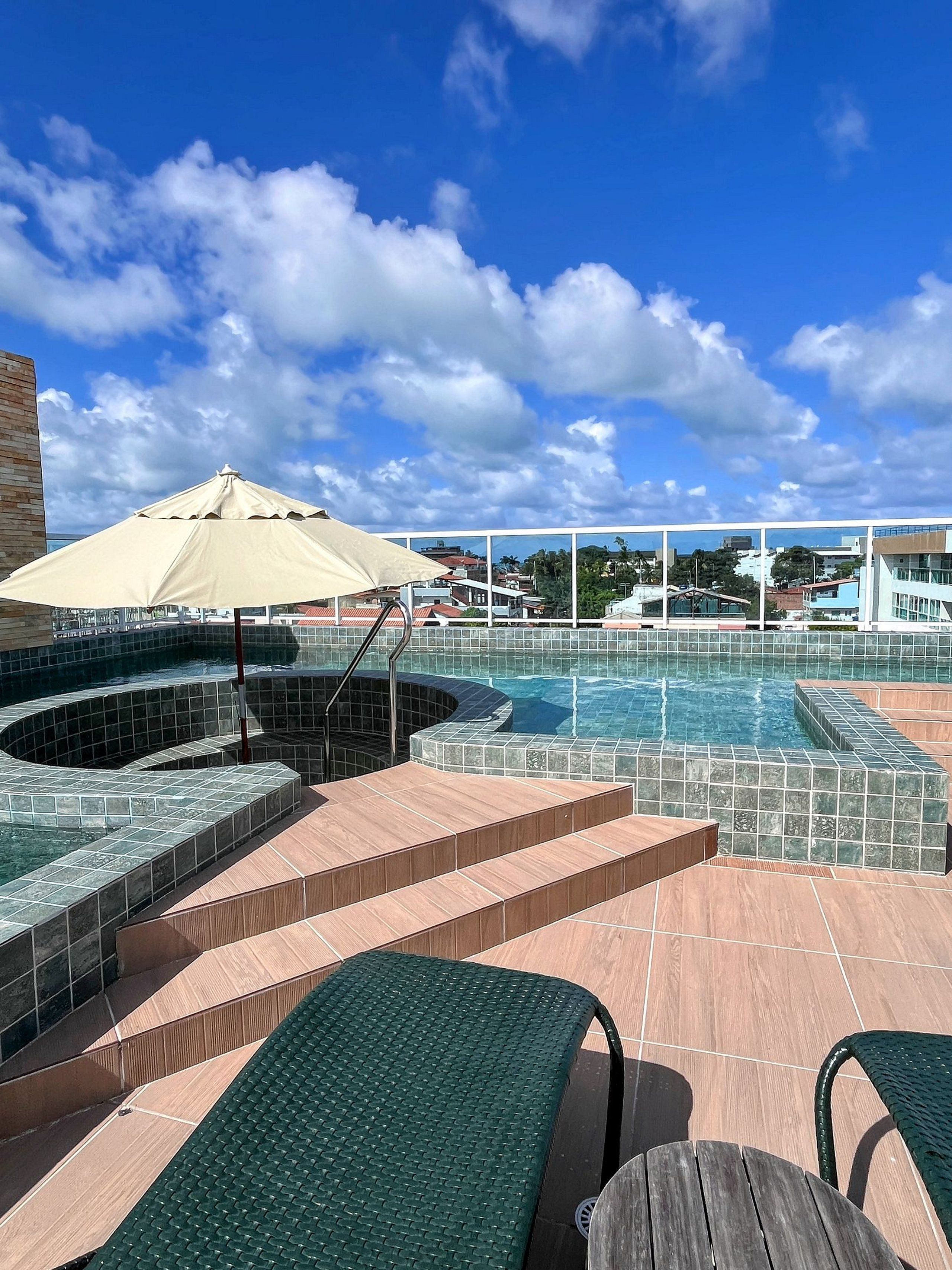 Un área de piscina en la azotea con sillones de descanso, una bañera de hidromasaje y vistas a la ciudad.