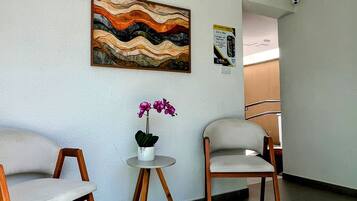 Una habitación con dos sillas, una mesita con una planta en maceta y una obra de arte colgada en la pared.