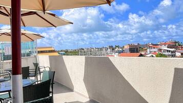 An outdoor seating area with tables and chairs under umbrellas, overlooking a cityscape with buildings and a clear sky.