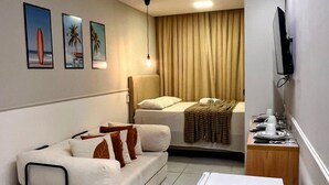 Habitación de hotel compacta con cama, sofá, refrigerador pequeño, televisión y obras de arte en la pared.