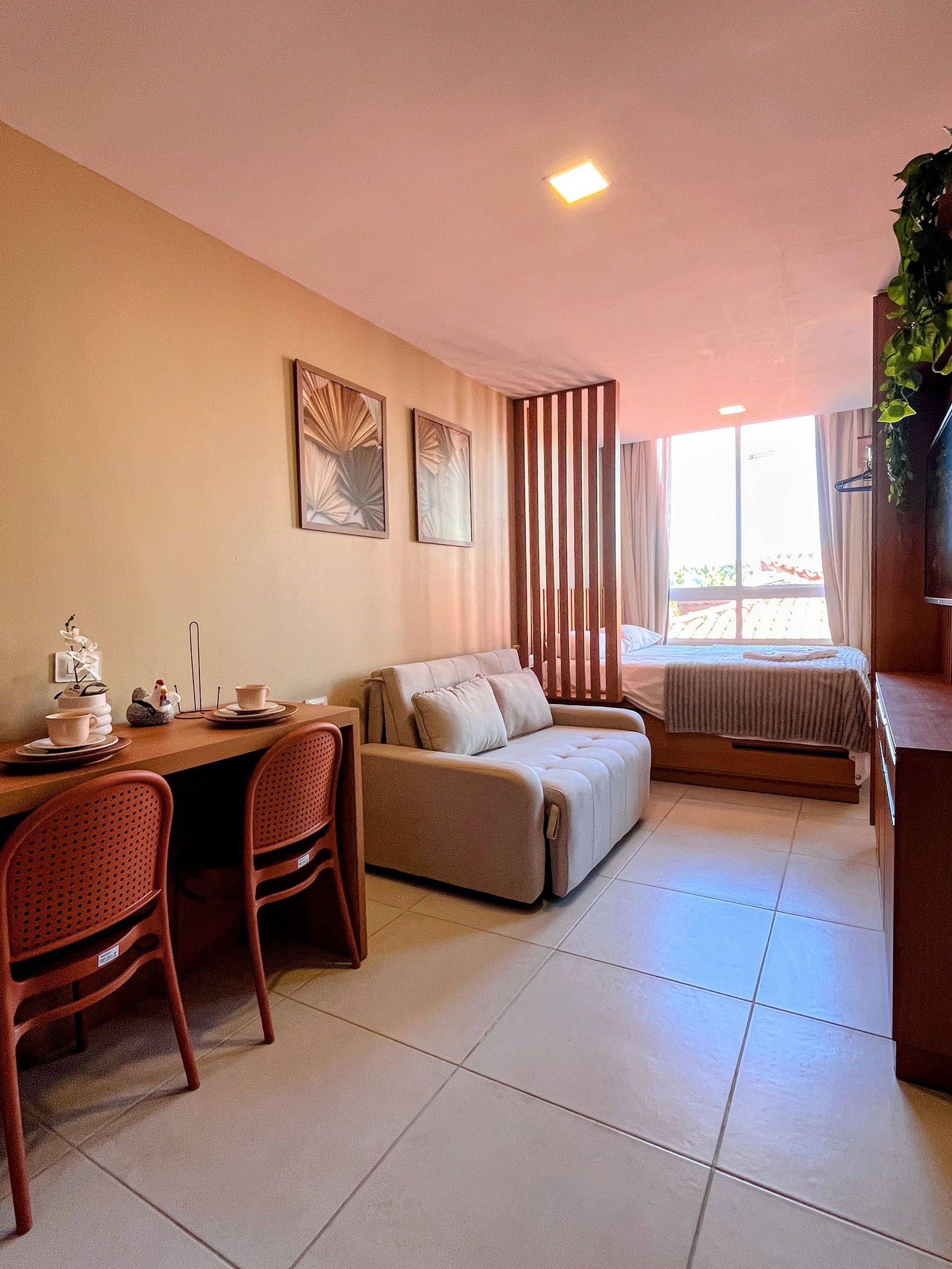 A modern living room with a sofa, a dining table with chairs, and a bed with a window view.