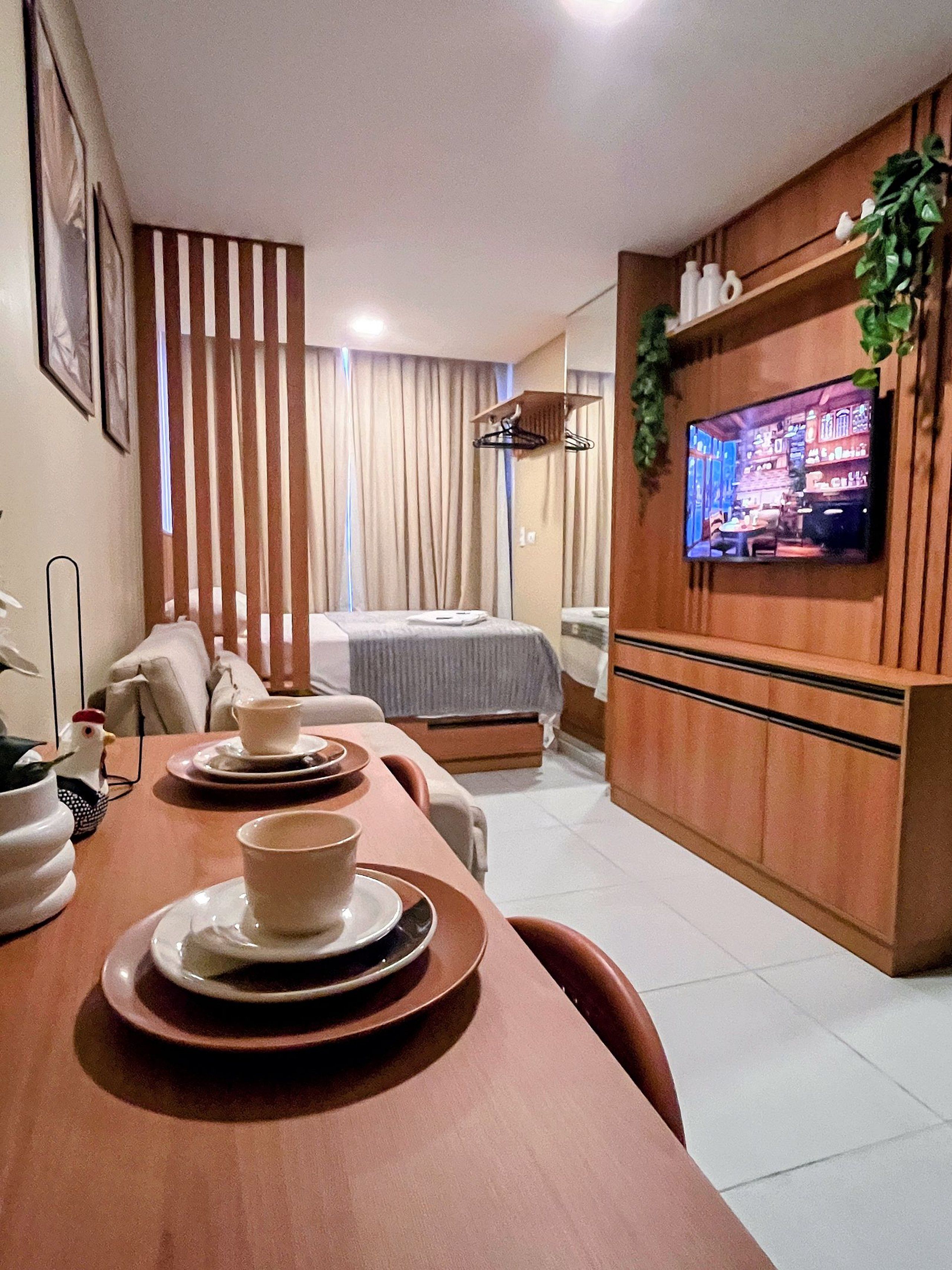 Habitación de hotel con zona de comedor, cama, televisor montado en la pared y ventana con cortinas.