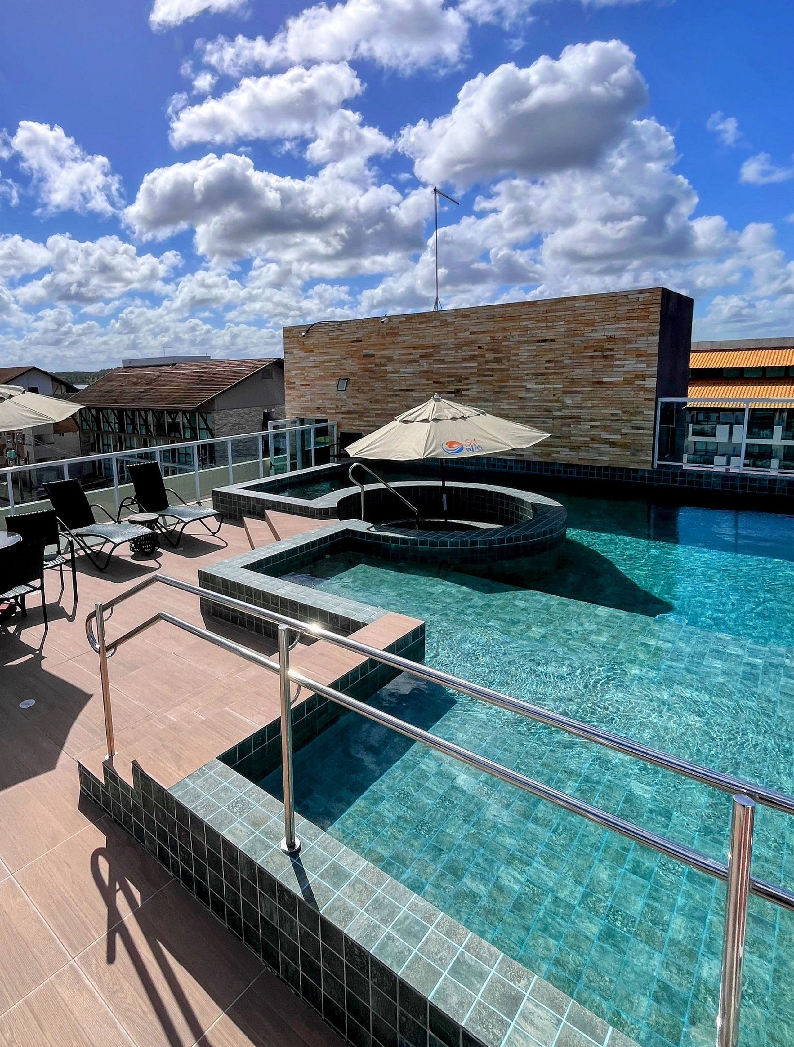 Zona de piscina con sillas de descanso y sombrillas, rodeada por un edificio con fachada de azulejos.