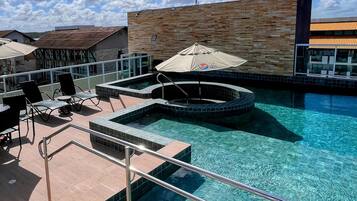 Zona de piscina con sillas de descanso y sombrillas, rodeada por un edificio con fachada de azulejos.
