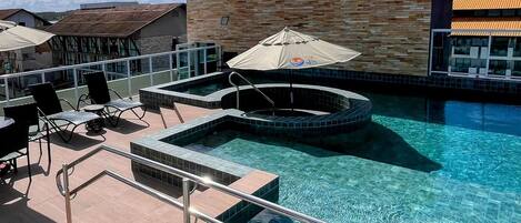 A swimming pool area with lounge chairs and umbrellas, surrounded by a building with a tiled exterior.