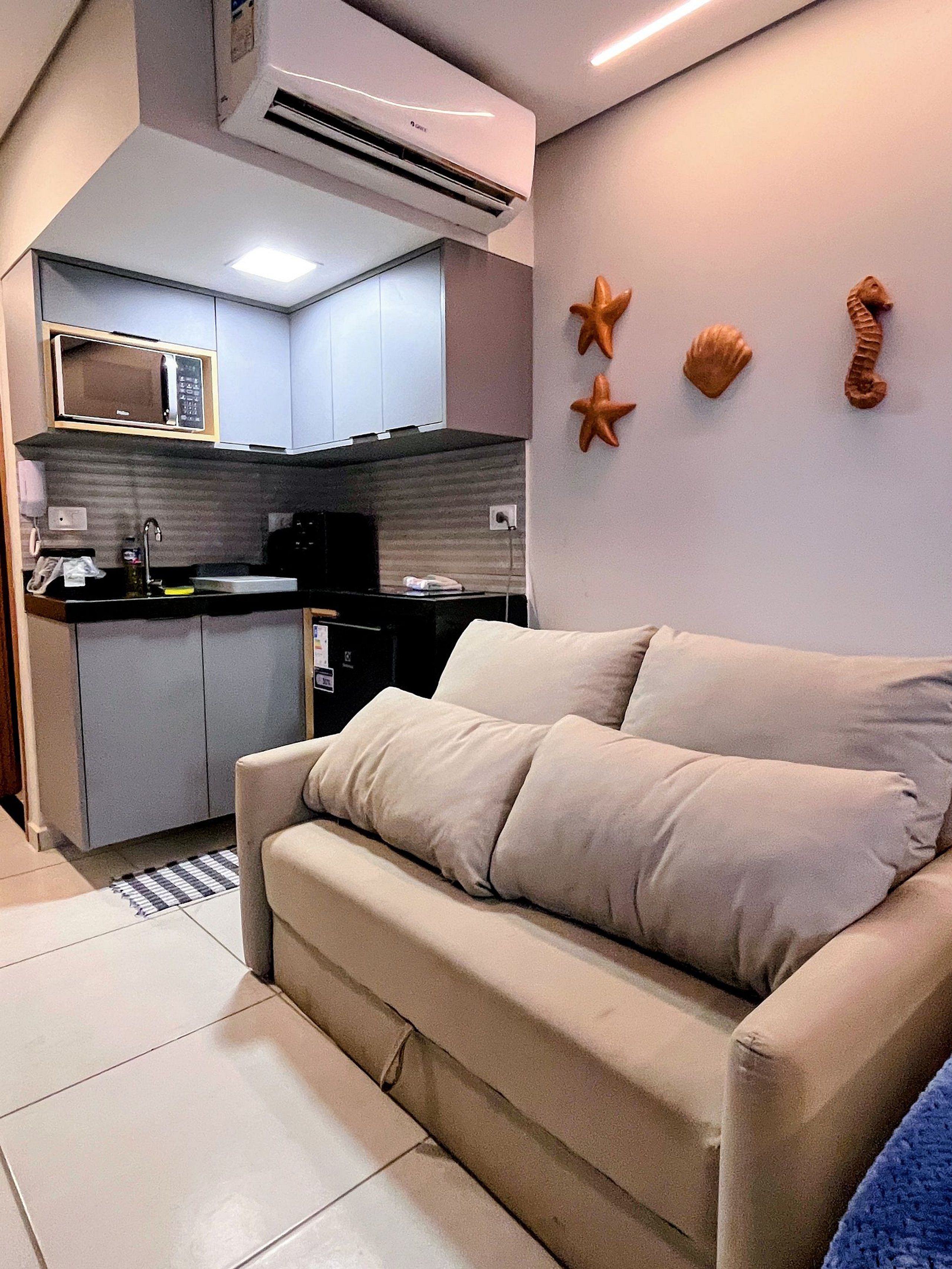 A modern kitchen with a microwave, stove, and sink. There is a beige sofa with pillows and a striped rug in the living area.