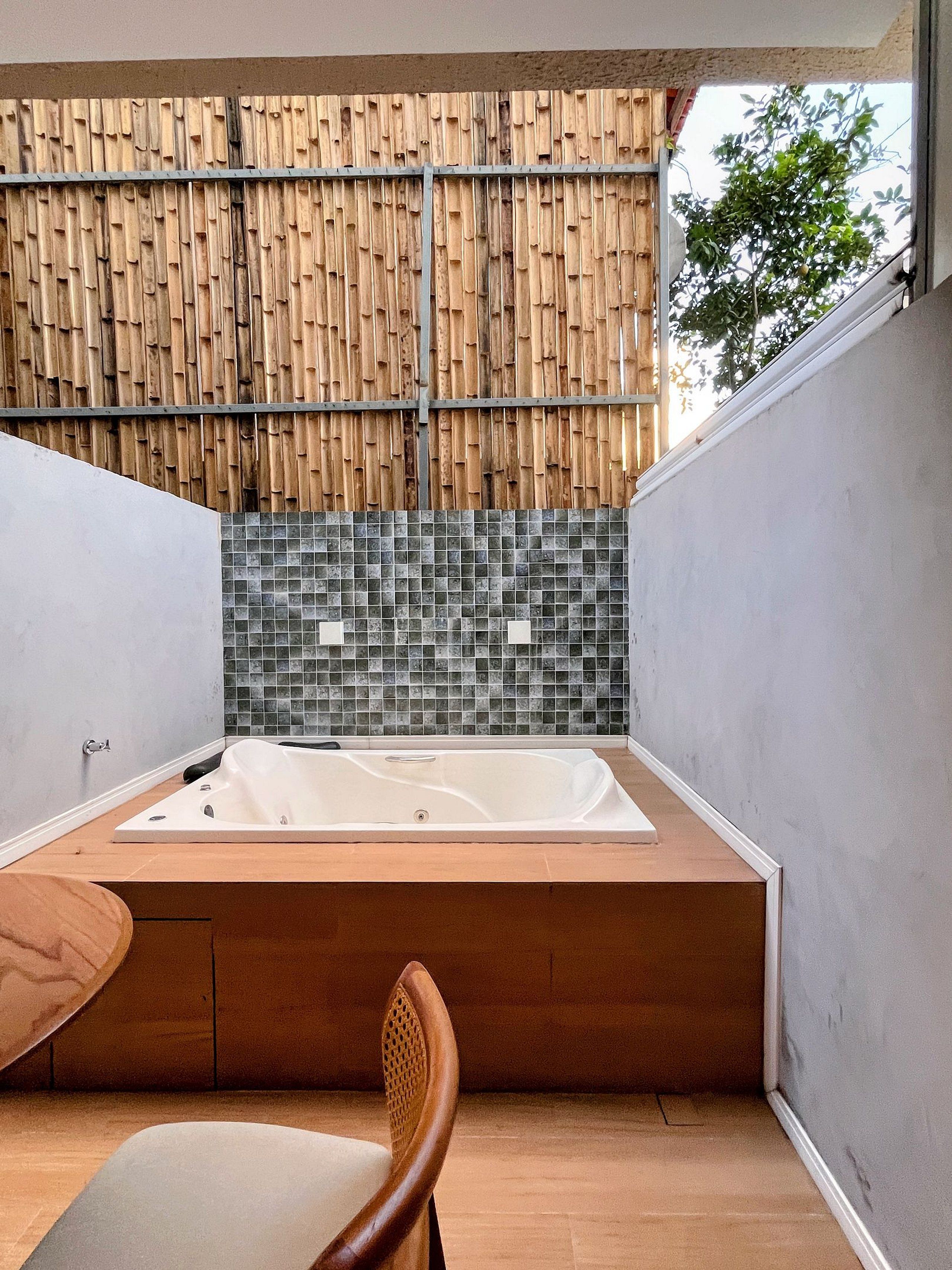 Ett modernt badrum med ett stort badkar, en trästol och en väggpanel av bambu.