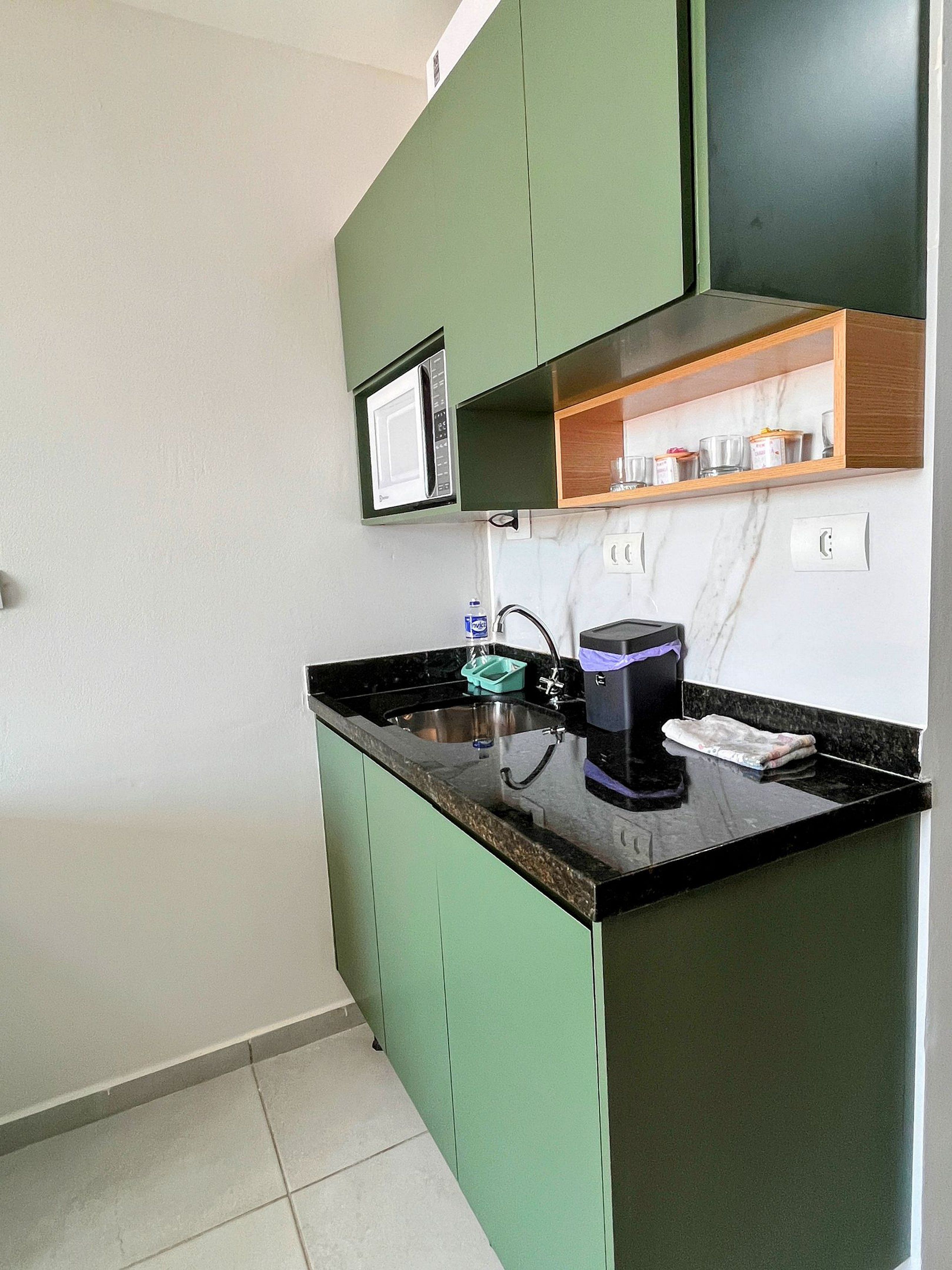 Cocina compacta con microondas integrado, cafetera y estante con cristalería.