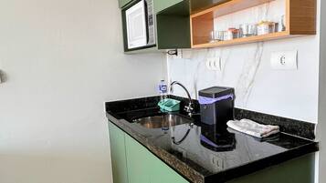 Cocina compacta con microondas integrado, cafetera y estante con cristalería.