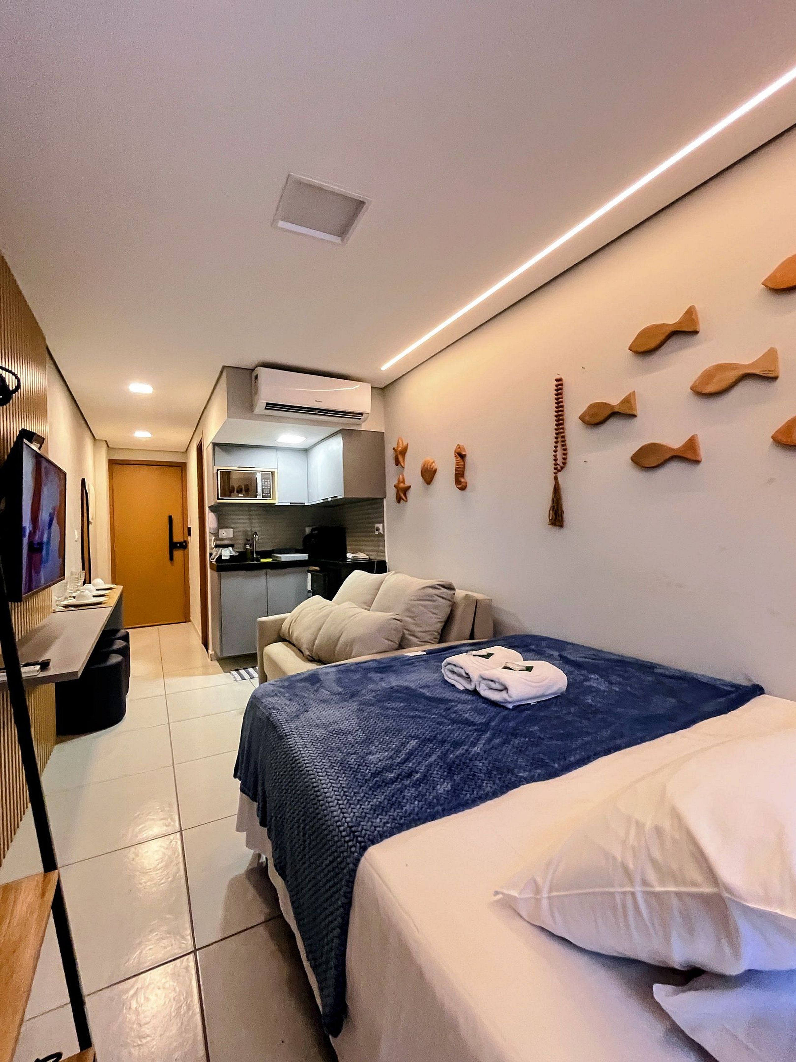 A hotel room with a bed, a TV, a kitchenette, and a wall with fish-shaped decorations.