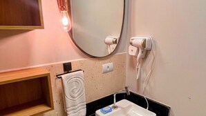 Un baño con lavamanos blanco, un espejo, un secador de pelo, toallero y un inodoro.