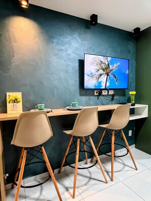Uma área de refeições moderna com uma TV fixada em uma parede escura, uma mesa de madeira e três cadeiras com pés de madeira.
