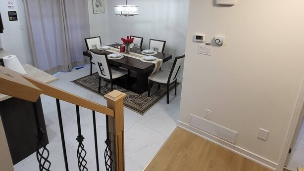 Un'elegante sala da pranzo moderna con una scala in legno, un lampadario e un tavolo imbandito per quattro persone.